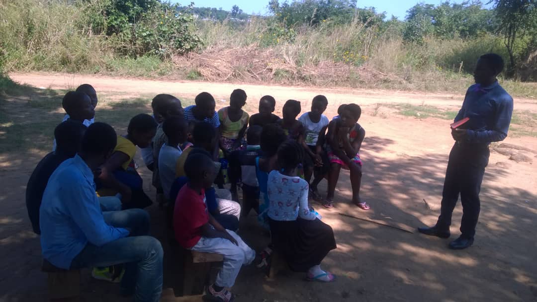 A facilitator leading a seated outdoor discussion with children.