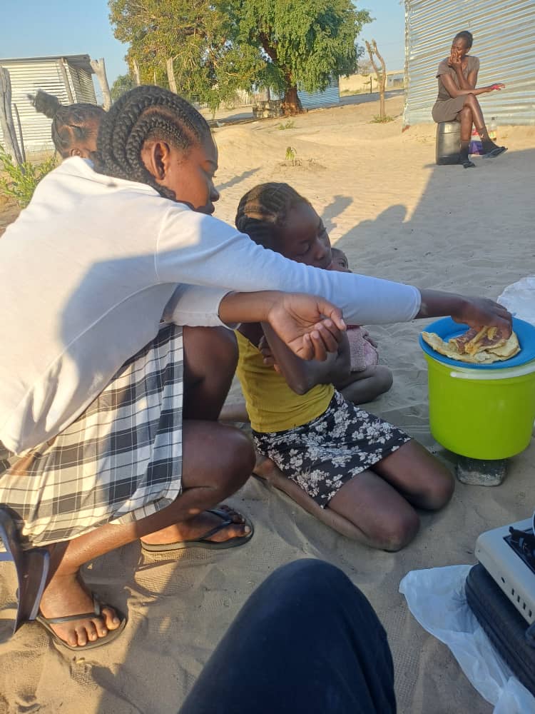 A caregiver serving food to children during an outdoor community activity.