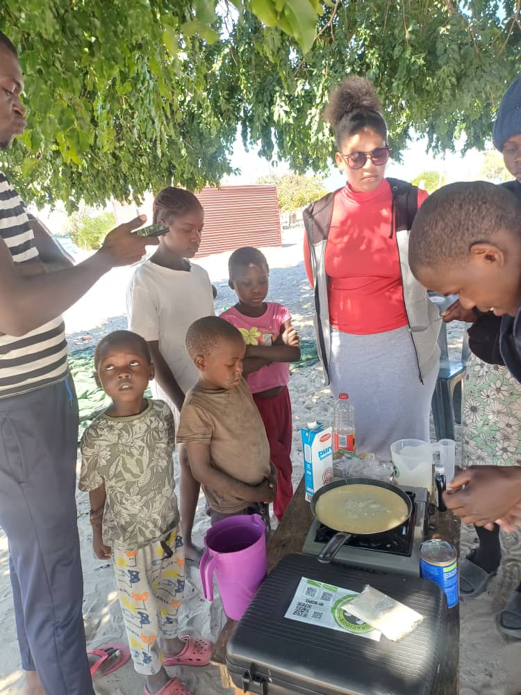 Children and caregivers gathered around a portable stove during a cooking activity.